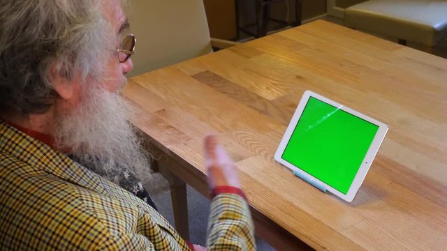 Older man with beard talking to greenscreen tablet