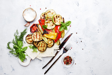Grilled colorful vegetables, aubergines, zucchini, pepper with spice and green basil on serving board on white background, top view