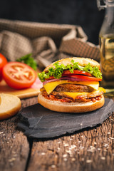 delicious fresh home made burger with lettuce, cheese, onion and tomato on black stone and wood background