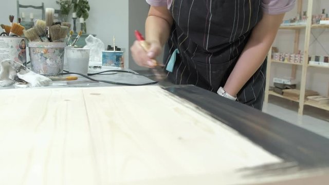 The woman in the workshop is working on wooden boards, creating an effect of antiquity