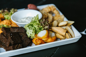 Meat plate with pork ribs, chicken, fried potatoes, cheese balls, croutons, sausages with sauce on black background