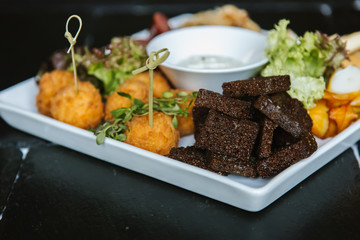 Meat plate with pork ribs, chicken, fried potatoes, cheese balls, croutons, sausages with sauce on black background
