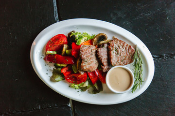 Pork steak with mushrooms, tomatoes, cucumbers, pepper, sauce on a black background