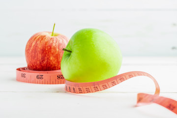 Red and green apples with measuring tape on white table