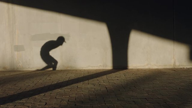 dancing man shadow of young break dancer performing hand stand freestyle dance moves fit mixed race male practicing in city at sunset