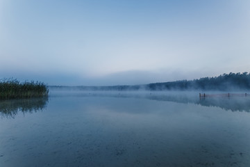 Fog over the lake, twilight over the lake, very dense fog, dawn, blue sky over the lake, the morning comes, the forest reflects in the water, surface water, clear morning sky, gothic, Grim picture