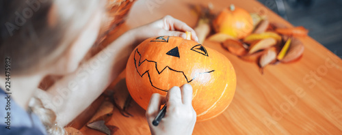 Preparation for Halloween: woman hands paint orange pumpkin with black paint. Closup. Holiday decoration concept.