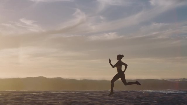 silhouette woman running on beach waves splashing female athlete runner exercising sprinting intense workout on ocean seaside at sunset