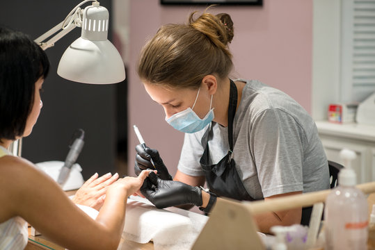 The process of manicure in a beauty salon.  The manicure master in black  gloves makes the processing of nails to the woman with the specialized equipment.