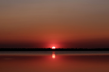 Beautiful, red dawn on the lake. The rays of the sun through the fog. The blue sky over the lake, the morning comes, the sky is reflected in the water.