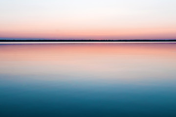 Beautiful, red dawn on the lake. The rays of the sun through the fog. The blue sky over the lake, the morning comes, the sky is reflected in the water.