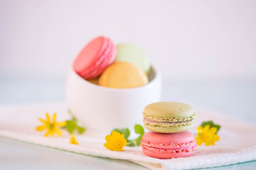 Fototapeta na wymiar Macarons in white porcelain bowl with nice yellow flowers on blue wooden table