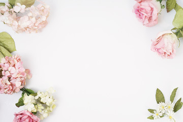 Frame made of pink and beige roses, green leaves, branches on white background. Flat lay, top view. Wedding's background