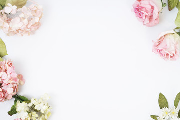 Frame made of pink and beige roses, green leaves, branches on white background. Flat lay, top view. Wedding's background