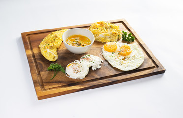 Healthy breakfast with poached egg, scrambled eggs, omelette on wooden plate 
