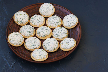 Snack on crackers with cheese is located on a plate on a dark background, top view