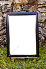 Easel staying om grass and moss near ancient stone walll with copy space