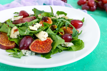 Classic salad with figs, arugula, blue cheese, grapes on a white plate. Tasty vegetarian dish. Close up