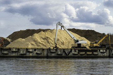 Pile of sand on a sea port, two yellow and white cranes truck with a sand hill at the construction area
