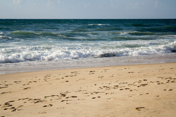 Seascape, blue waves with white foam on the beach with golden sand under a blue sky