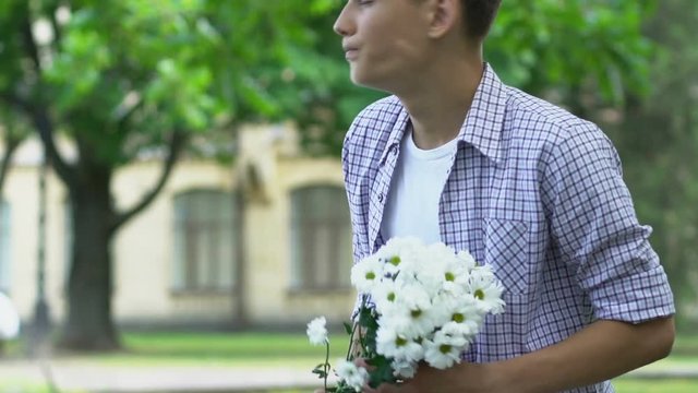 Boy holding flowers, waiting for girlfriend on date, nervous, insecure teenager