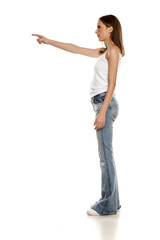 Young pretty woman posing in bell bottom jeans on white background, and pointing on empty space