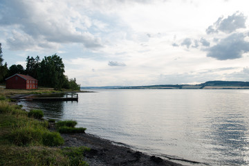 scenic view of Mjosa lake under cloudy sky and distant red cottage, Hamar, Hedmark, Norway