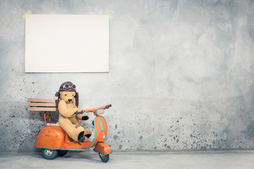 Teddy Bear in leather pilot's helmet sitting on old retro orange toy scooter with pizza boxes  in...