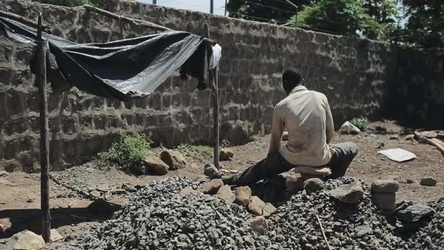 Back View Of Man From Africa Works At Construction Site. Guy Is Sitting On The Quarry