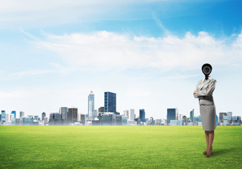 Camera headed woman standing on green grass against modern cityscape