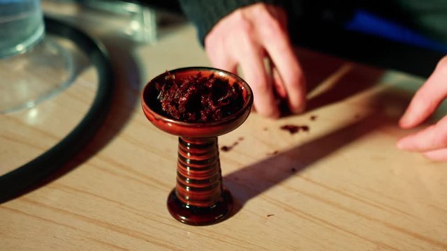 Hookah master prepares hookah. He clogs the tobacco in the bowl.