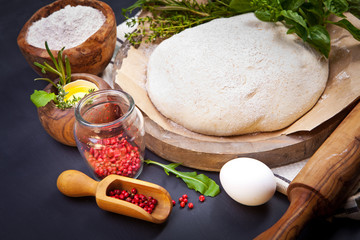 Wooden rolling pin with freshly prepared dough and dusting of flour on dark background
