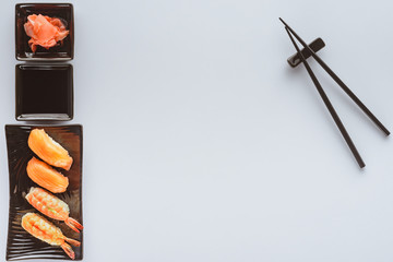 top view of delicious sushi with salmon and shrimp, ginger and chopsticks isolated on white background