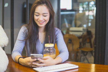 Beautiful young asian woman in the cafe, using mobile phone and drinking coffee smiling.