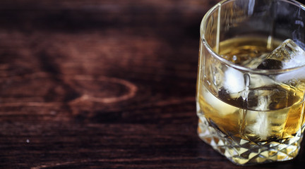Whiskey with ice with a glass. Cubes of ice on a wooden table an