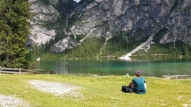 Young girl sitting near by beautiful lake in the mountains, Lago Di Braies Italy