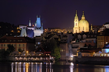 Scenic view of night Prague. Vltava river with many cafes and restaurants in the buildings on the river bank. Medieval buildings of old town at the background at summer night. Prague, Czech Republic