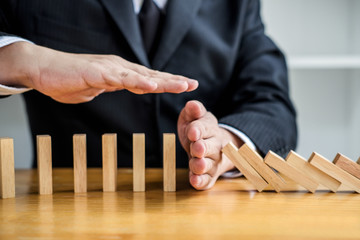 Wooden game strategy, Businessman hand stopping falling wooden dominoes effect from continuous...