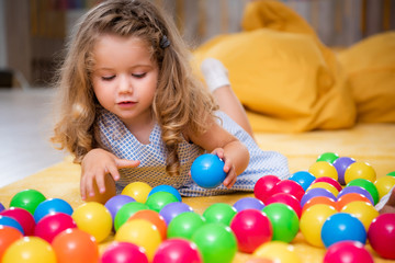 adorable child lying on carpet and playing with colorful balls in kindergarten