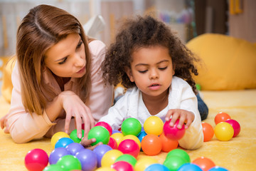 tutor and adorable african american child playing with colorful balls in kindergarten
