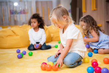 adorable multiethnic children playing with colored balls on floor in kindergarten