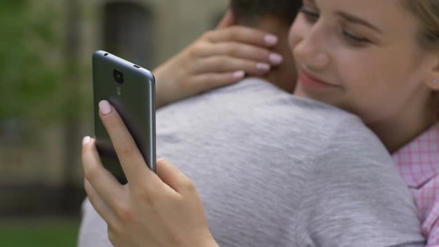 Girl texting on smartphone while embracing boyfriend, lie and betrayal, closeup