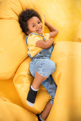 high angle view of smiling african american boy lying on bean bag chairs and looking at camera in...