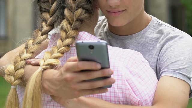 Boy texting on smartphone while embracing girlfriend, lie and betrayal, closeup
