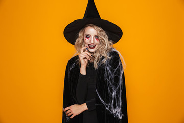 Image of tricky witch woman wearing black costume and halloween makeup looking at camera, isolated...