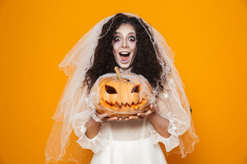 Image of dead bride zombie on halloween wearing wedding dress and scary makeup holding carved...