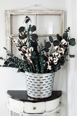 Old olive bucket filled with eucalyptus and cotton stem arrangement on a farmhouse table in front...