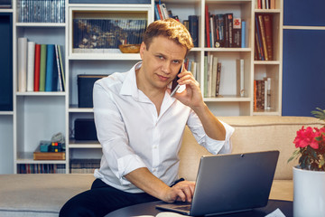 Fototapeta premium Handsome businessman in white shirt sitting in front of laptop and speaking over phone. Business concept.