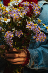 A girl dressed in jeans holds wild flowers in her hands