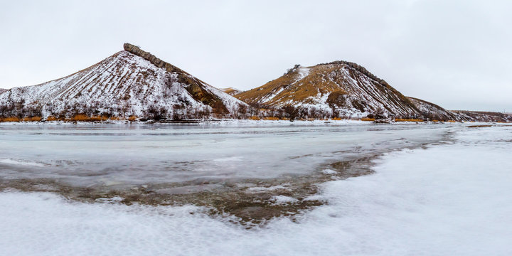 The panoramic snowy view with two rocky hills and the ice surface of the winter river. Two Sisters mountain, Belaya Kalitva town, Seversky Donets river, Russia